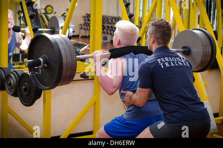 Personal trainer helping young male client in gym during workout on equipment. Stock Photo