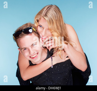 happy teenage couple piggybacking, smiling - isolated on blue. Stock Photo