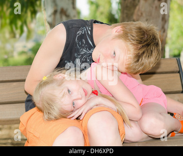 Two kids brother and sister curled up together on the bench in park Stock Photo