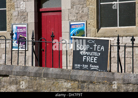 Handwritten sign mounted on metal fence with red door in background. Stock Photo