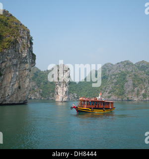 A view of a tourist boat moving by the spectacular limestone karst formations in Lan Ha Bay, Halong Bay, Vietnam. Stock Photo