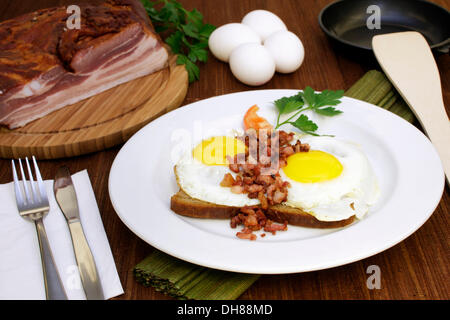 Fried eggs with fried bacon bits on bread, tomato slice, Italian parsley, raw eggs Stock Photo