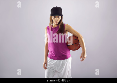 Confident young woman holding basketball. Beautiful caucasian female basketball player on grey background Stock Photo