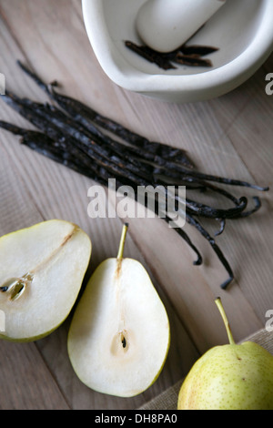 Pestle and mortar, whole Madagascan vanilla pods and pears on a wooden chopping board Stock Photo
