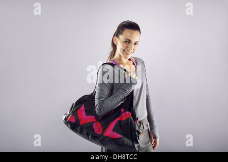 Happy fit young woman with gym bag standing ready for fitness exercise. Young caucasian female going for gym looking at camera Stock Photo