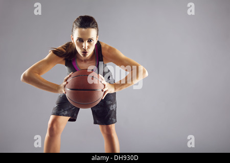 Portrait of young female basketball player passing the ball. Beautiful caucasian woman in sportswear playing basketball on grey Stock Photo