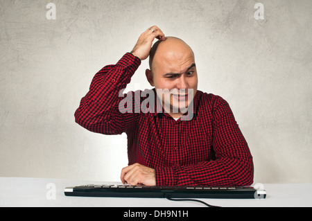 Confused man sitting at office table in front of the computer keyboard. Computer problem. Stock Photo