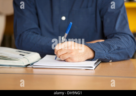 Male Student Writing In Book At Library Stock Photo