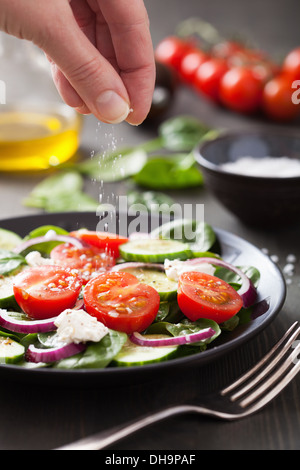 hand adding salt to vegetable salad Stock Photo