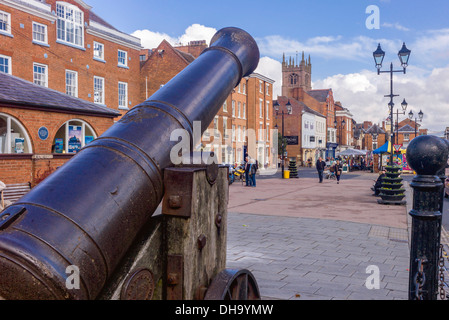 A large cast iron cannon is pointing over market square Ludlow whilst shoppers are busy looking on the colourful market stalls