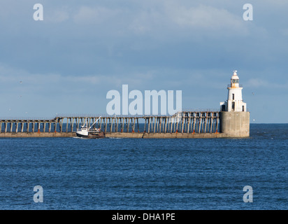 Fishing boat entering Blyth harbour passing lighthouse and pier pier, Northumberland, England, UK Stock Photo