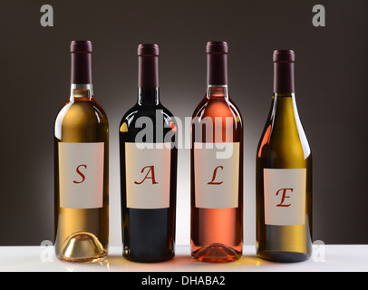 Four Wine Bottles with their labels spelling out the word SALE on a light to dark gray background. Stock Photo