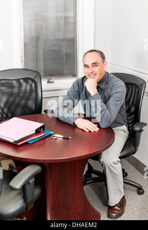 Middle aged business man looking happy sitting at table in office meeting room Stock Photo
