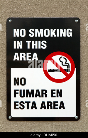 Bilingual no smoking sign with graphic and written in the English and Spanish languages is screwed to a wall. Stock Photo