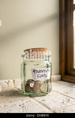 Glass jar labeled Adventure Fund containing loose change. Stock Photo
