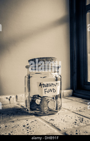 Glass jar labeled Adventure Fund containing loose change. Stock Photo