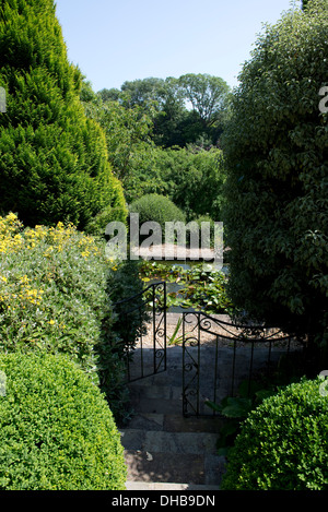 Garden steps through shrubs leading down through a gate to a pond Stock Photo