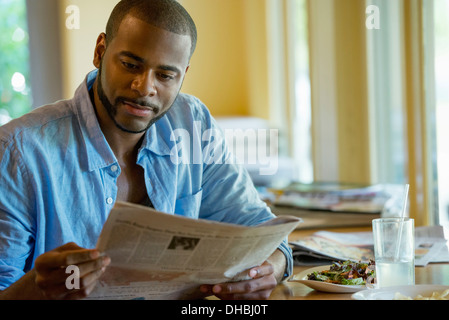 A man sitting along in a cafe, reading a newspaper. Stock Photo