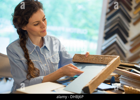 A woman in a picture framer's workshop, choosing frames and cardboard mounts. Surrounded by samples. Stock Photo