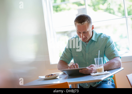 A man with short cropped hair sitting at a cafe table. Using a digital tablet. Stock Photo