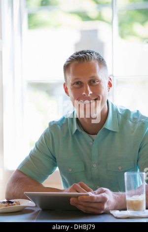 A man with short cropped hair sitting at a cafe table. Using a digital tablet. Stock Photo