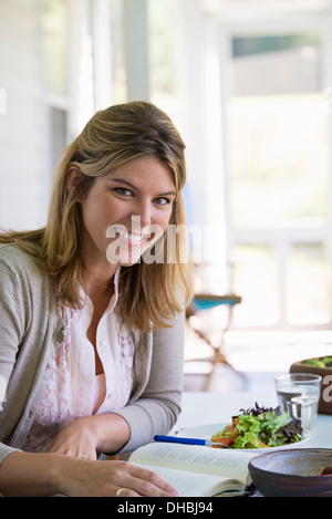 A woman sitting at a table reading a book. Stock Photo