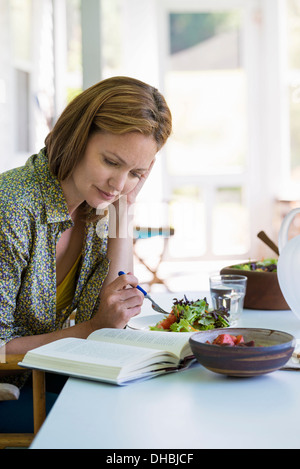 A woman sitting at a table reading a book. Stock Photo