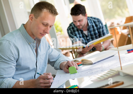 Two men seated at a table using books and a digital tablet. Stock Photo