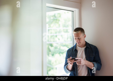 A man standing in a quiet corner of a cafe, using a smart phone. Stock Photo