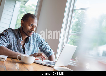 A man sitting in a cafe with a cup of coffee, using a laptop computer. Stock Photo