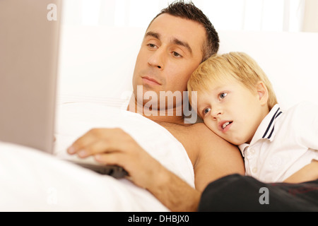 Father and son surfing on their computers on the bed at home Stock Photo