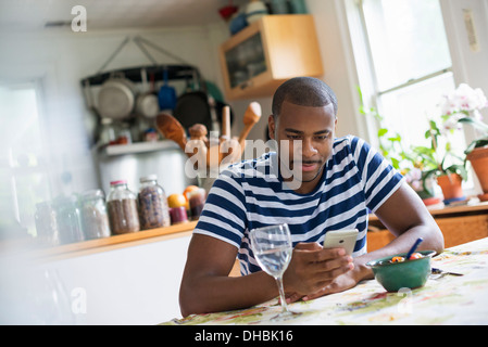 A man sitting at a table using a smart phone. Fruit dessert and a glass of wine at hand. Stock Photo