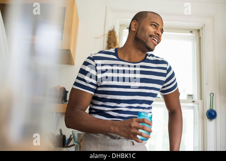 A man in a farmhouse kitchen holding a drink in a blue glass. Stock Photo