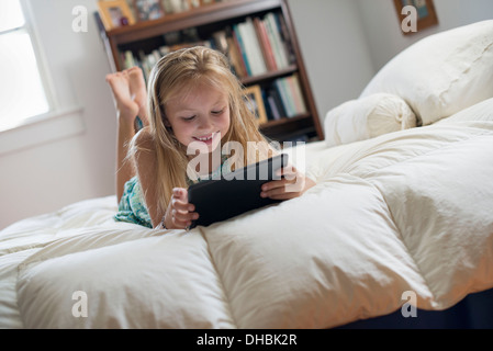 A young girl sitting on her bed using a digital tablet. Stock Photo