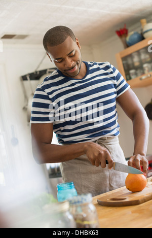 A man in a kitchen using a knife to slice an orange. Stock Photo