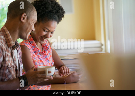 Two people using a digital tablet, seated close together at a cafe. Coffee cups. Stock Photo