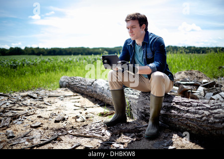 A farmer sitting using a tablet computer outdoors in a field of crops Stock Photo