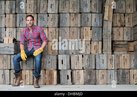 A farmyard. A stack of traditional wooden crates for packing fruit and vegetables. A man sitting on a packing case. Stock Photo