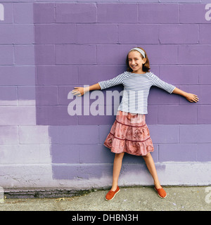 A ten year old girl in a tiered skirt, standing with her arms outstretched, leaning against a wall. Stock Photo