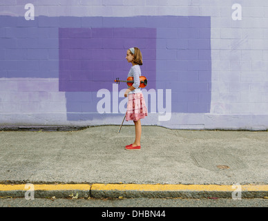 A ten year old girl holding a violin under her arm and a bow in her hand. Against a purple background. Stock Photo