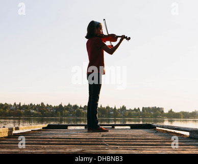 A ten year old girl playing the violin at dawn on a wooden dock. Stock Photo