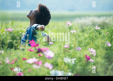 A woman standing among the flowers with her arms outstretched.  Pink and white cosmos flowers. Stock Photo