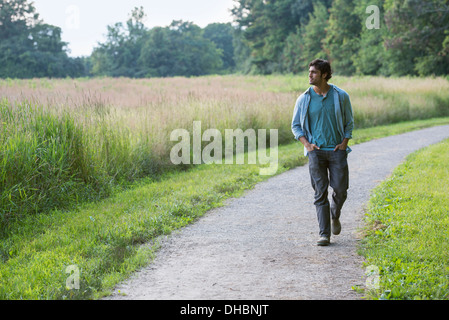 A young man walking down a path with his hands in his pockets. Stock Photo