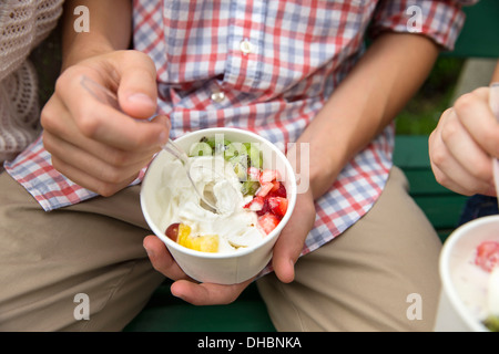 Young people sitting side by side, eating fresh organic fruit and yoghurt desert. Stock Photo