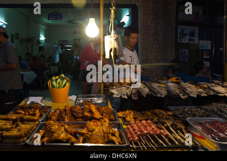 Horizontal portrait of a local Lao man barbecuing whole fish on a grill at a streetside cafe at night. Stock Photo