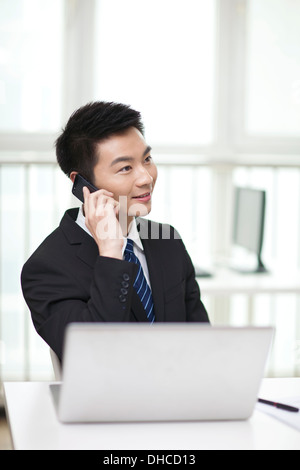 Portrait of businessman sitting at desk and using cell phone Stock Photo