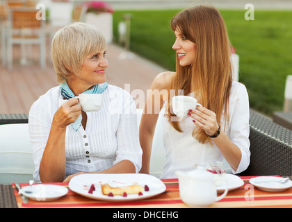 adult mother and daughter drinking tea or coffee and talking outdoors Stock Photo