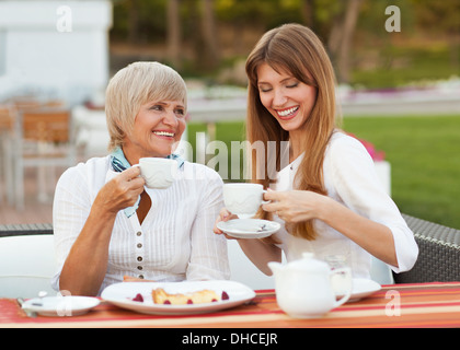 adult mother and daughter drinking tea or coffee and talking outdoors Stock Photo
