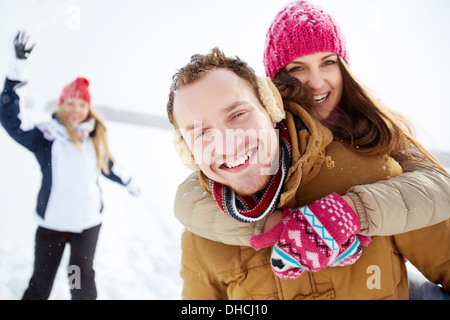 Portrait of happy young couple looking at camera in winter park with their friend behind Stock Photo