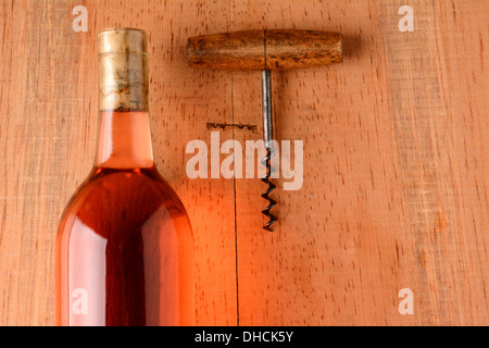 A blush wine bottle and corkscrew on a rustic wood surface with strong side light. Closeup in horizontal format with copy space. Stock Photo